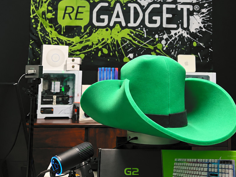 Regadget’s live show set: a big green foam cowboy hat in front of the Regadget banner, with a camera, microphone, a gaming PC and boxed keyboards on the desk.