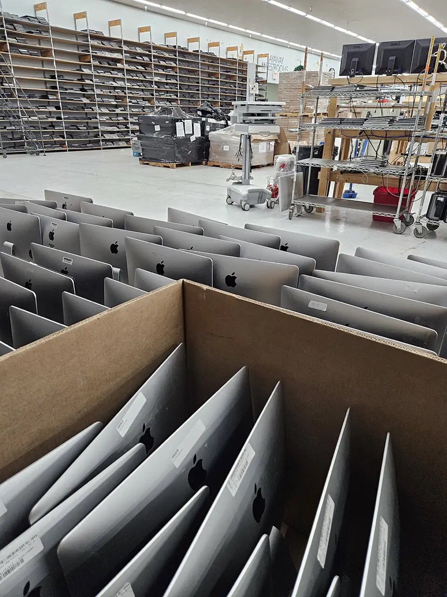 A cardboard lot of all-in-one desktops standing in dividers on our receiving floor, with wrapped pallets and shelving behind.