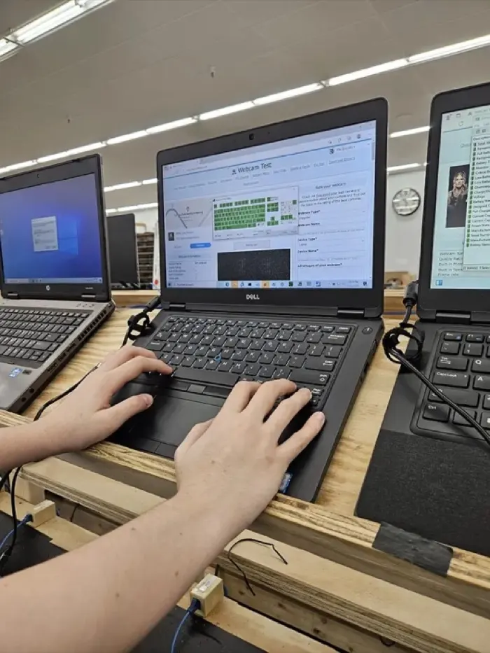 A technician testing a refurbished laptop’s keyboard and webcam on the bench.